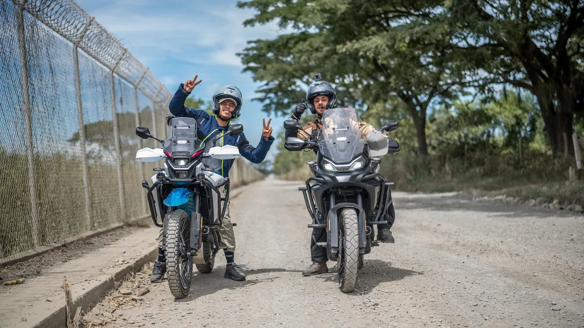 Dos motociclistas saludando a la cámara en una vía destapada
